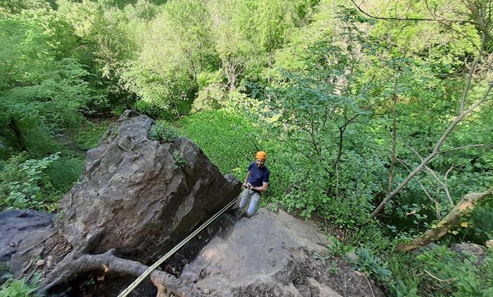 Man attached to rope abseiling down cliff
